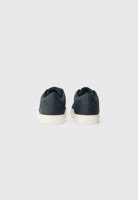 Sneakers noirs avec un panneau arrière texturé, semelle en caoutchouc blanche et col rembourré. Présentent une finition lisse et des détails de couture subtils.