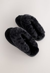 Chaussons noirs doublés de fourrure synthétique douce et à l'extérieur lisse. Conception à bout ouvert, forme arrondie et semelles plates pour plus de confort.