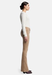 Beige fluwelen brede pijpen met een gladde textuur, gecombineerd met een aansluitende crèmekleurige longsleeve top en bordeauxrode block-heeled schoenen.