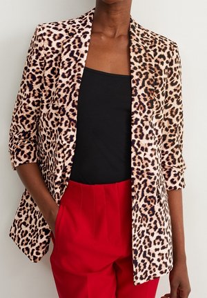 Blazer imprimé léopard avec manches retroussées sur un top noir, associé à un pantalon rouge taille haute, personne avec une main dans la poche.