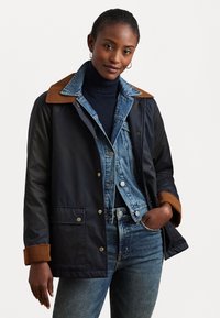 Navy jacket with brown collar and cuffs, featuring a button closure and front pockets. Worn over a denim shirt and blue jeans.