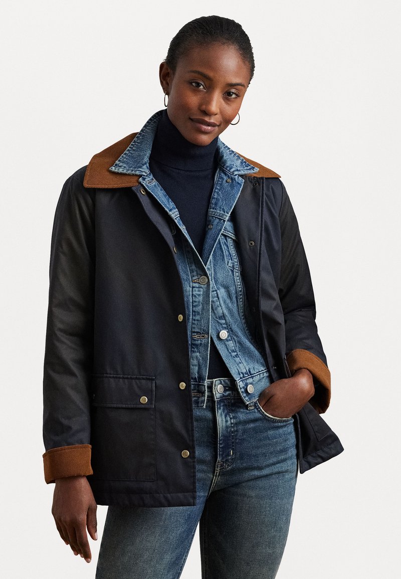 Navy jacket with brown collar and cuffs, featuring a button closure and front pockets. Worn over a denim shirt and blue jeans.