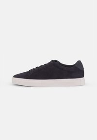 Navy suede sneaker with white rubber sole, rounded toe, lace-up closure, and contrasting heel accent, featuring a smooth texture.