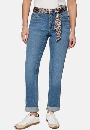 Frau trägt blaue Cuffed-Jeans mit einem Leopardenmuster-Stoffgürtel, der in der Taille gebunden ist, und weiße Sneakers mit beigen Sohlen.