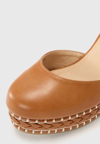 Zapato de plataforma de cuero marrón con punta redonda y un detalle de textura trenzada en la suela, resaltado por costuras blancas en contraste.