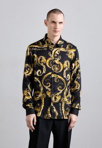 Camicia nera con bottoni, decorata con un motivo dorato a vortice, realizzata in tessuto morbido. Presenta un colletto classico e maniche lunghe.