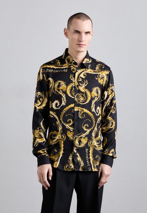 Camicia nera con bottoni, decorata con un motivo dorato a vortice, realizzata in tessuto morbido. Presenta un colletto classico e maniche lunghe.
