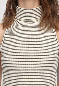 Top senza maniche a righe con colletto alto. Il tessuto è di colore chiaro con righe orizzontali nere, creando un aspetto texturizzato.
