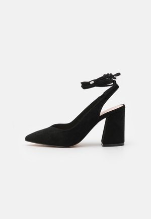 Escarpin en suède noir à talon haut, bout pointu, talon bloc, arrière ouvert et bride de cheville nouée en nœud.