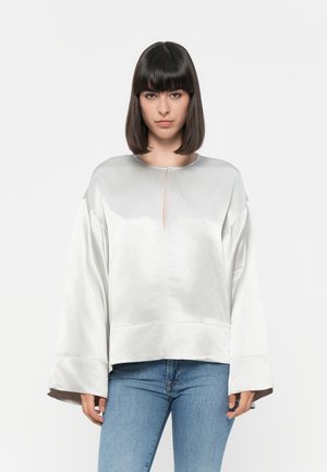 Sølv satinbluse med lett shimmer, rund hals, droppede skuldre og brede, lange ermer. Har en liten frontslitt.