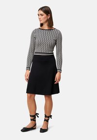 Zwarte jurk met een aangesloten, gemêleerd langemouwen top en een uitlopende rok. Bevat zwarte ballerina's met enkelbandjes.