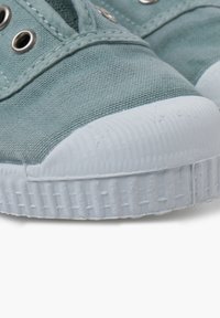 Plátěné tenisky v jemné zelené barvě s texturovaným povrchem, s bílou gumovou špičkou a kontrastními očky na šněrování. Uzavřený design šněrování.