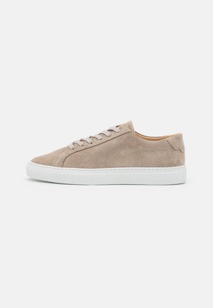 Beżowy zamszowy niskoprofilowy sneaker z białą gumową podeszwą i pasującymi beżowymi sznurówkami, pokazany z profilu na białym tle.