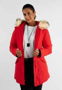 Parka rouge avec capuche en fausse fourrure, fermeture éclair à l'avant et fermetures à pression. Dispose de deux poches avant et d'une silhouette ajustée.