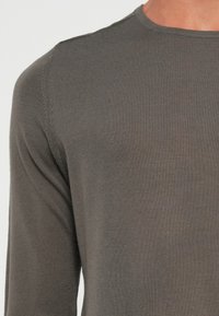 Long-sleeve, dark grey ribbed knit shirt with a round neckline. Soft texture and visible stitching detail on the seams and sleeves.