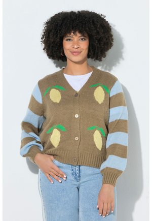 Kvinde med krøllet hår iført en brun cardigan med citronmønstre og blå striber på ærmerne, kombineret med lyseblå jeans.