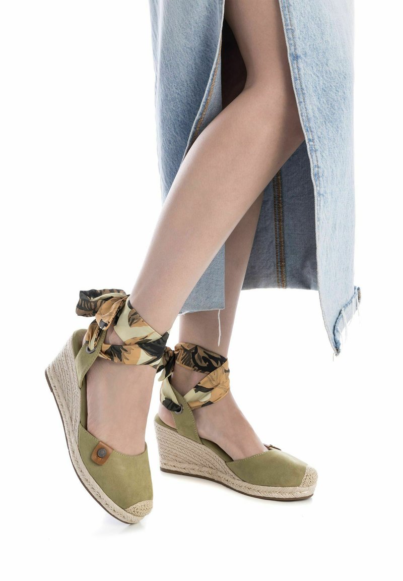 Le sandali con tacco a zeppa in suede verde presentano una suola in juta, cinturini alla caviglia in tessuto floreale decorativo e una punta arrotondata con una parte anteriore intrecciata.