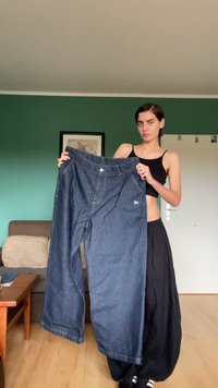 Široke temno modre kavbojke iz denima z gumbom in sprednjimi žepi, z majhnim logotipom blizu pasu. Gladka tekstura.