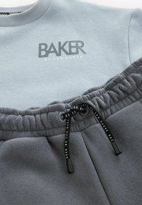 Lys grå sweatshirt med "BAKER BY TED BAKER" logo, parret med mørke grå sweatpants med elastisk talje og snøre.