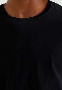 Camiseta negra de cuello redondo hecha de una suave mezcla de algodón, con un ribete en el cuello y una textura suave y uniforme sin patrones visibles.