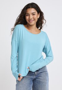 Jasnoniebieska koszula z długim rękawem, wykonana z miękkiego materiału, z okrągłym dekoltem i luźnym krojem, z otworami na kciuki w mankietach. Para niebieskich dżinsów.