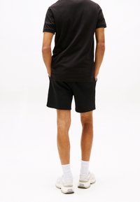 Svart bomullströja och svarta shorts, sedd bakifrån. Sneakers och vita strumpor är synliga. Enkel, avslappnad design.