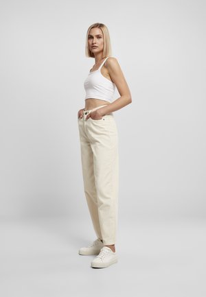Pantalones de talle alto en beige claro con un corte relajado, combinados con una camiseta sin mangas blanca y zapatillas blancas. Diseño sencillo, estilo casual.