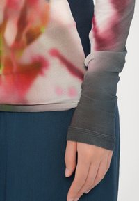 Langärmliges Oberteil mit einem Farbverlauf-Design und floralen Mustern in rosa, rot und grünen Farbtönen, kombiniert mit dunklen Ärmeln und Bündchen.
