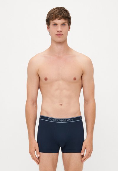Marineblaue Herrenbadehosen mit einem elastischen Bund, auf dem das Emporio Armani-Logo zu sehen ist. Der Stoff wirkt glatt, mit einer taillierten Passform und ohne sichtbare Muster.