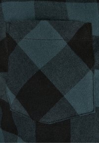 Gros plan sur un tissu à carreaux noir et bleu sarcelle foncé avec une poche carrée cousue assortie au motif.