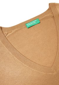 Sweter z dekoltem w serek w jasnobrązowej dzianinie, z ribbowanym wykończeniem dekoltu. Na metce napis "United Colors of Benetton" w kolorze zielonym.