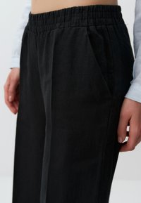 Zwarte, high-waisted, linnenmix broek met een elastische tailleband, zijzakken en een ontspannen pasvorm. Gladde textuur en een wijde pijpdesign.