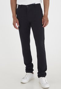 Pantaloni in cotone blu navy con taglio dritto, due tasche anteriori, chiusura con bottone e passanti per cintura, abbinati a sneakers bianche.