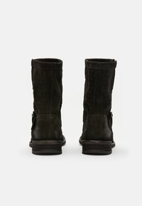 Black suede ankle boots feature a rounded toe and textured surface, with a low stacked heel and side strap detailing.