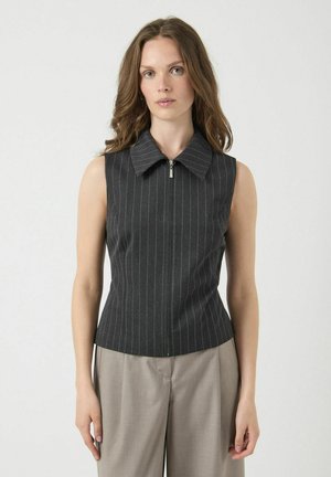 Haut noir à rayures sans manches avec une coupe structurée, dotée d'un col pointu et d'une fermeture éclair à l'avant. Texture de tissu lisse.