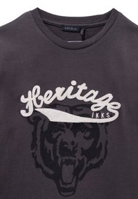 T-shirt di cotone grigio scuro con logo "Heritage" ricamato e grafica di un orso in nero. Collo rotondo e maniche corte.