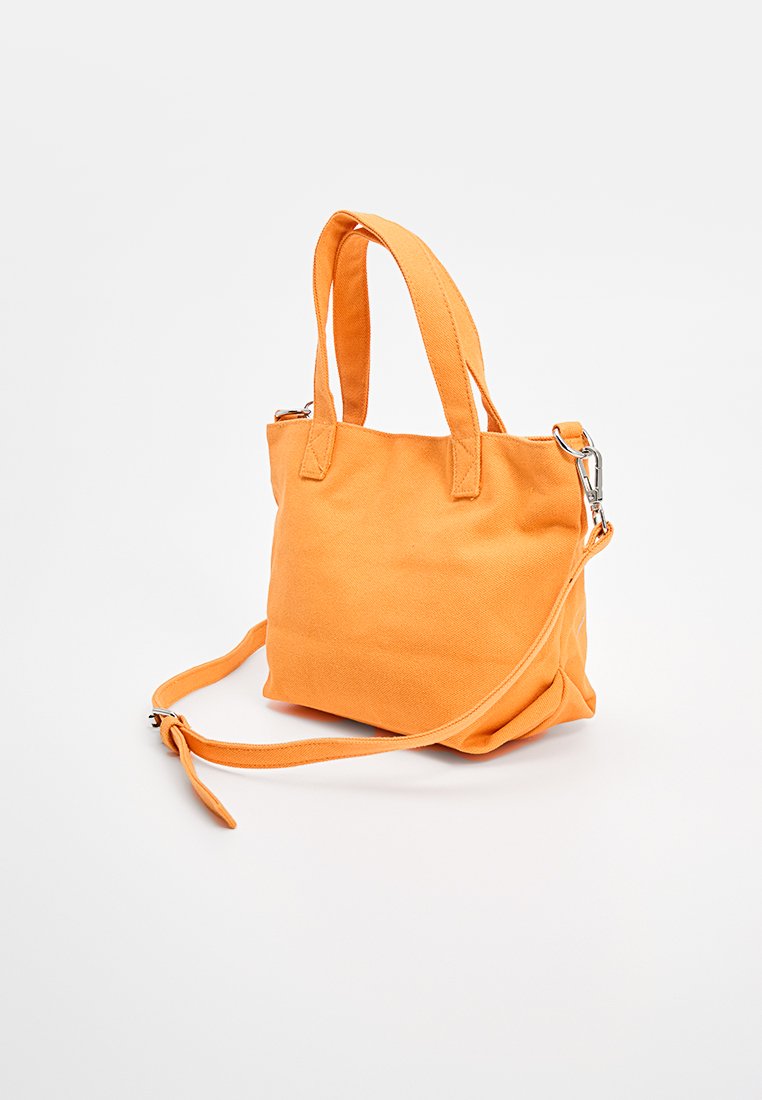 Bolso tote de lona naranja con dos asas cortas y una correa de hombro desmontable, que presenta una forma rectangular y una tela texturizada resistente.