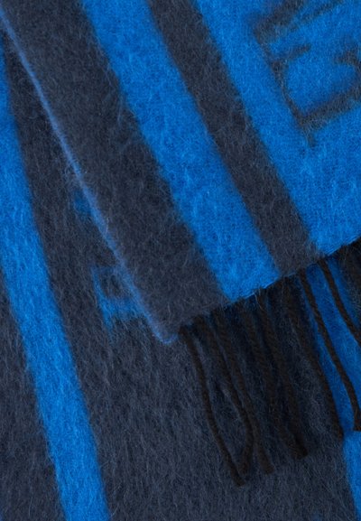 Tissu doux tissé bleu et gris foncé avec franges, montrant un motif géométrique et une texture duveteuse.