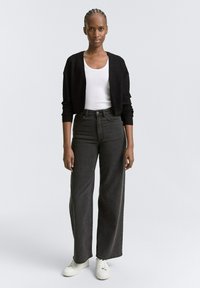 Schwarze Strickjacke, weißes, enges Tanktop, hoch taillierte, dunkelgraue, weit geschnittene Jeans und weiße Sneakers. Glattes Material mit minimalen Details.