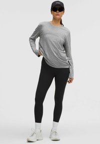 Maglietta sportiva grigia a maniche lunghe abbinata a leggings neri e scarpe da ginnastica bianche. Include un cappellino nero e occhiali da sole. Texture della stoffa liscia.
