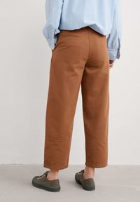 Bruine katoen wijduitlopende broek met een schone zoom, achterzakken en een middelhoge taille. Gecombineerd met olijfgroene sneakers.