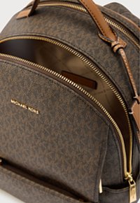 Sac à dos en tissu marron texturé avec des accents dorés, doté de compartiments zippés et de bretelles en cuir marron, détail du logo à l'avant.