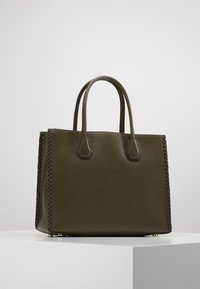 Mörkgrön läder tote-väska med två korta handtag, som har flätade detaljer på sidorna och metallfötter för stabilitet.