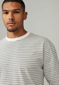 Stribet pullover skjorte i hvid og sort, med korte ærmer og rund hals. Glat bomuldsstruktur med jævne vandrette linjer.