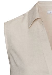 Beige linen blouse with a collar, sleeveless design, and a V-neck opening. Smooth texture and subtle stitching detail at the edges.