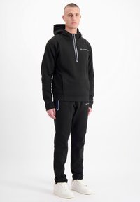 Zwarte sporthoodie met een ritssluiting aan de voorkant en grijze accenten, gecombineerd met zwarte joggers. Gemaakt van zachte stof, met een relaxte pasvorm en zijzakken.