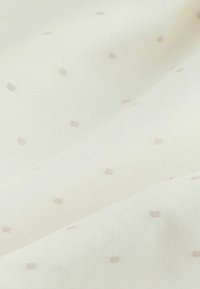 Țesătură din bumbac de culoare crem deschis cu mici modele pătrate roz, dispersate, prezentând o textură netedă și un design subtil.