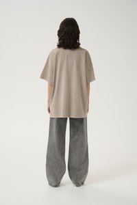 Oversized beige cotton t-shirt with a round neckline, short sleeves, and straight cut, paired with loose gray denim pants.