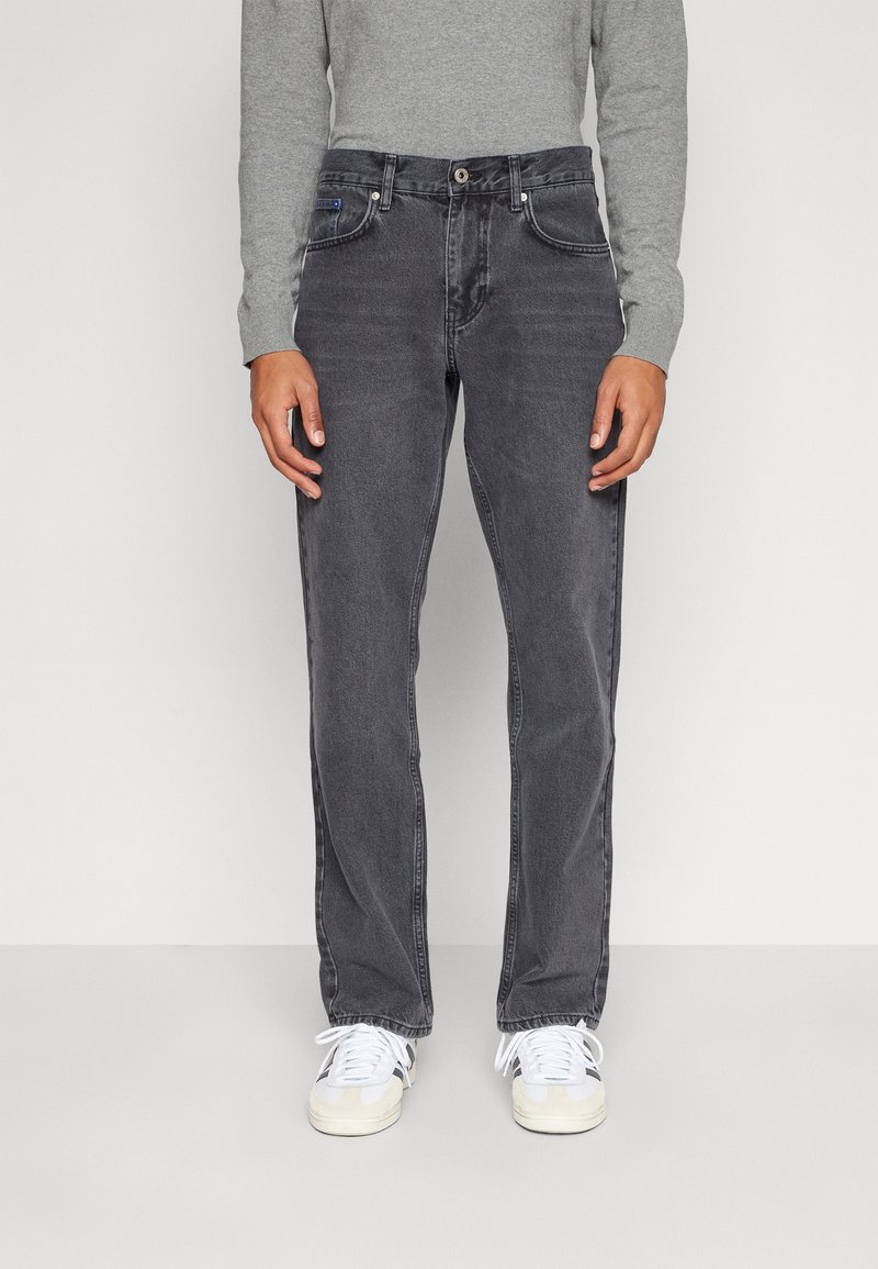 Jeans da uomo in denim grigio con taglio dritto, design a cinque tasche e dettagli di sbiaditura sottili. Abbinati a sneaker bianche e una maglietta grigia a maniche lunghe.