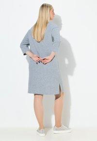 Šedé pletené šaty s tříčtvrtečními rukávy, bočním rozparkem a kulatým výstřihem, nošené se stříbrnými třpytivými teniskami. Hladká textura.